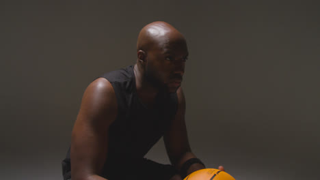 Studio-Portrait-Shot-Of-Seated-Male-Basketball-Player-With-Hands-Holding-Ball
